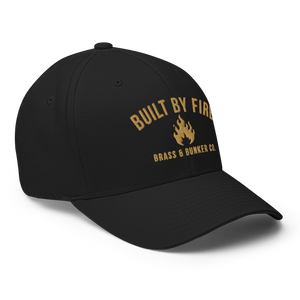 A black baseball cap with gold embroidered text reading 'BUILT BY FIRE' and 'BRASS & BUNNER CO.' around a small flame graphic on the front, shown on a clean white background.