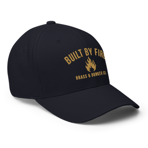 A black baseball cap with gold embroidered text reading 'BUILT BY FIRE' and 'BRASS & BUNNER CO.' around a small flame logo on the front, shown on a clean white background.