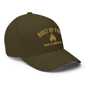 An olive green baseball cap with gold embroidered text reading 'BUILT BY FIRE' and 'BRASS & BUNKER CO.' around a small flame logo on the front, shown on a clean white background.