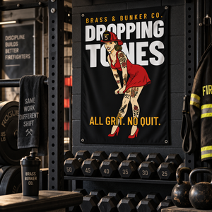 Black gym banner featuring a tattooed firefighter pin-up with “BRASS & BUNKER CO. DROPPING TONES” and “ALL GRIT. NO QUIT.”
