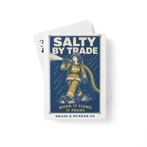 A stack of playing card deck fanned out on a white background. The top card features a vintage-style illustration of a firefighter in yellow gear spraying water, with the text 'SALTY BY TRADE' and 'BRASS & BUNKER CO'.
