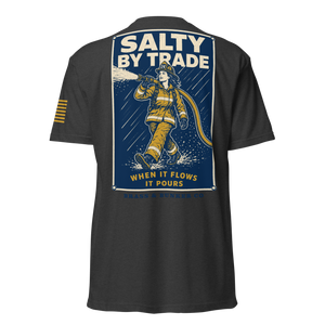 A dark charcoal gray t-shirt shown from the back, featuring a large graphic print of a firefighter in yellow gear spraying water under a blue sky, with the text 'SALTY BY TRADE' and 'WHEN IT FLOWS IT POURS'.