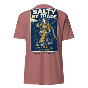 A dusty rose short-sleeve t-shirt shown from the back, featuring a large graphic print of a firefighter with the text 'SALTY BY TRADE WHEN IT FLOWS IT POURS' and 'BRASS & BUNKER CO' on a dark blue background.