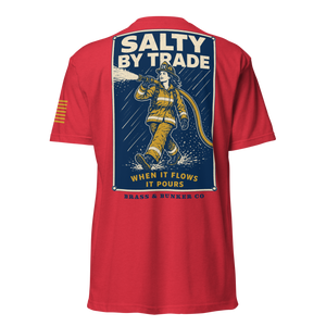 A red short-sleeve t-shirt shown from the back, featuring a large graphic print of a firefighter with the text 'SALTY BY TRADE WHEN IT FLOWS IT POURS' and 'BRASS & BUNKER CO' on a white background.