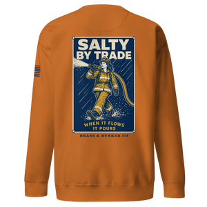 An orange crewneck sweatshirt shown from the back, featuring a large graphic print of a firefighter with the text 'SALTY BY TRADE' and 'BRASS & BUNKER CO'.