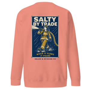 A coral pink crewneck sweatshirt shown from the back, featuring a large graphic print of a firefighter with the text 'SALTY BY TRADE' and 'BRASS & BUNKER CO'.