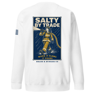 White crewneck sweatshirt shown from the back, featuring a large graphic print of a firefighter in yellow gear on a dark blue background with the text 'SALTY BY TRADE' and 'BRASS & BUNKER CO'. A small blue striped logo is visible on the left sleeve.