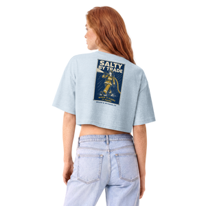 A woman with red hair is shown from the back wearing a light blue cropped t-shirt with a vintage-style 'Salty by Trade' graphic on the back, paired with light-wash jeans, against a plain white background.