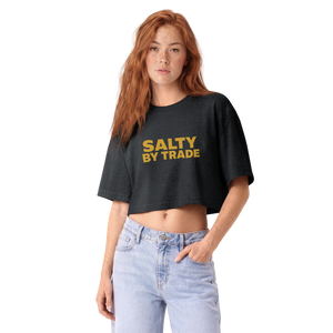 A woman with red hair wearing a dark charcoal gray cropped t-shirt with 'STAY SALTY' printed in yellow across the chest, paired with light blue jeans, against a plain white background.